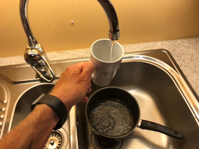 En hånd som holder en kopp over vasken og fyller på vann fra kranen.