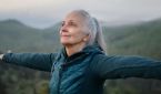 Eldre dame ute på fjelltur som står med armene ut og nyter livet