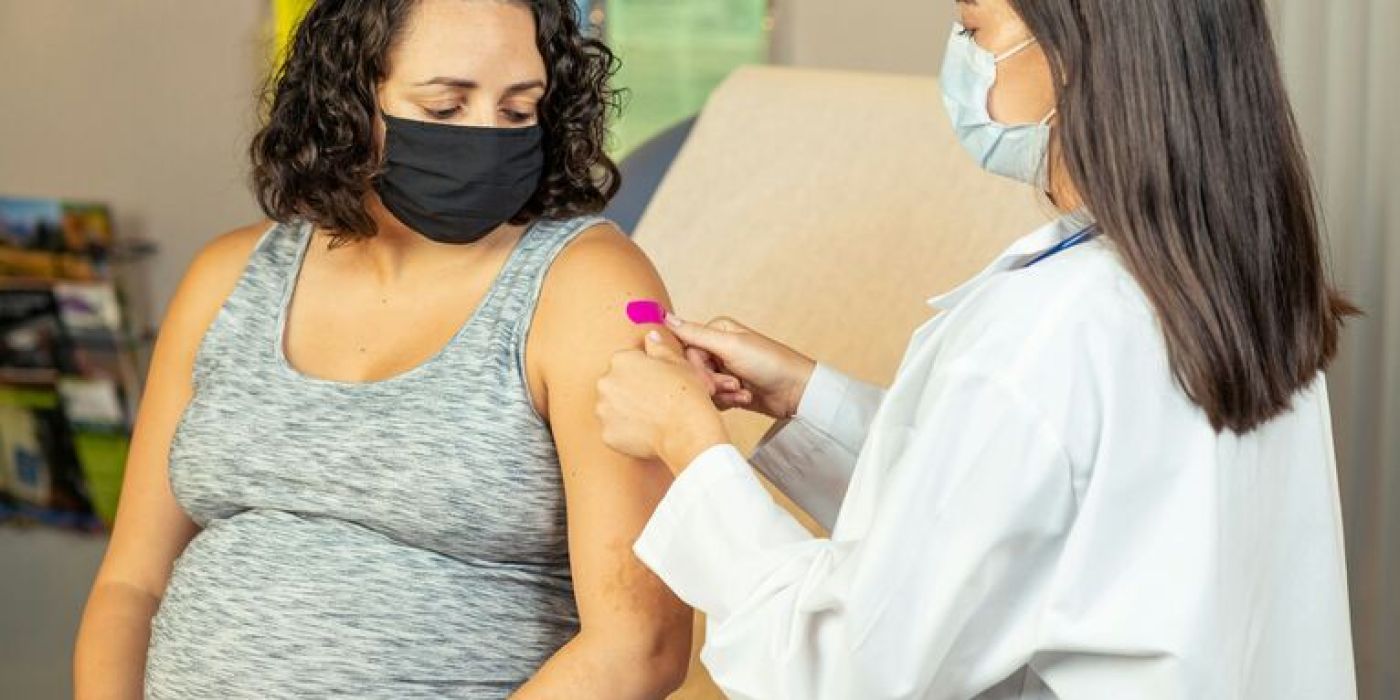 Gravid dame som får vaksine. Både mor og legen har munnbind på