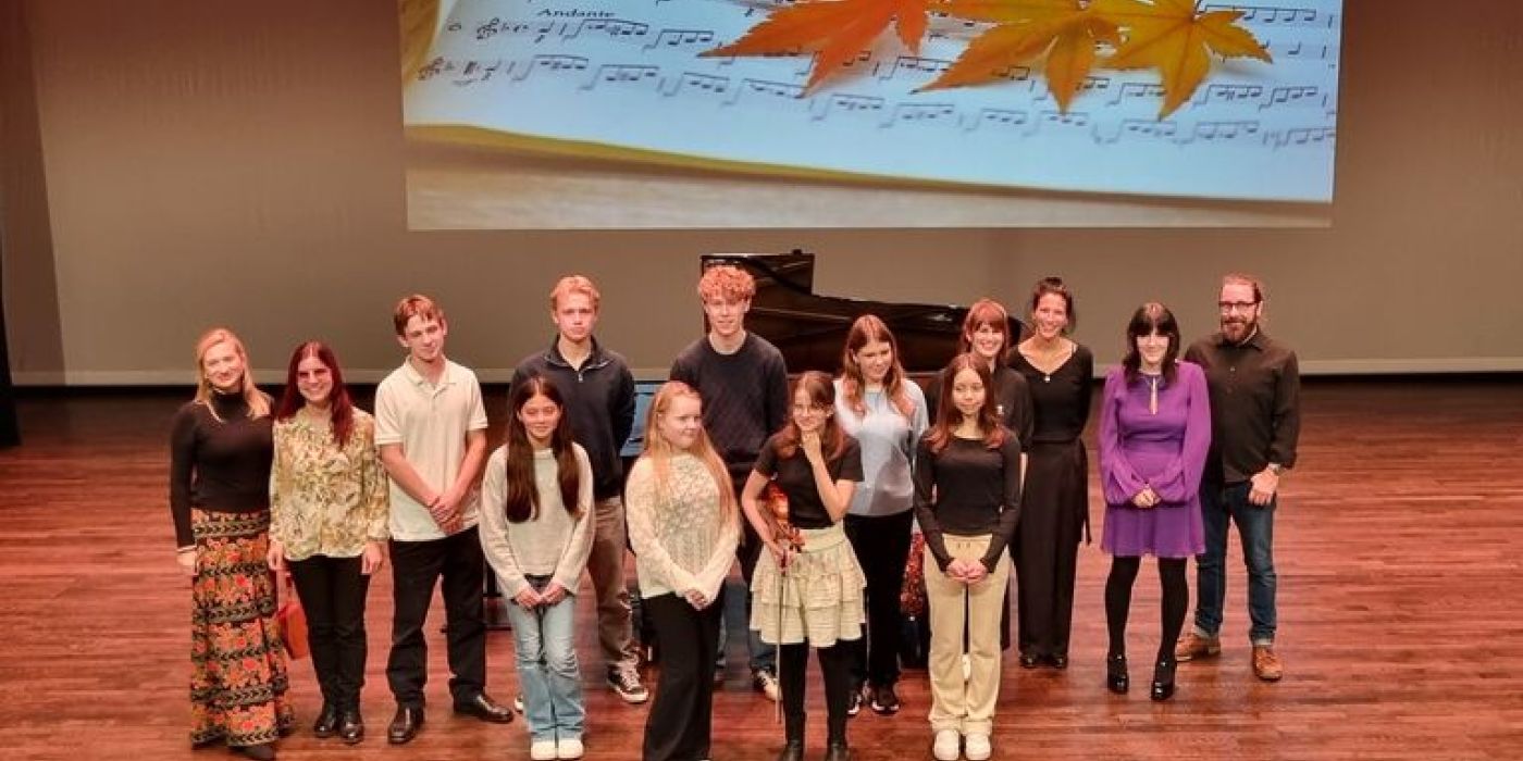 en scene med flygel og skjerm i bakgrunnen. Fremme står elever og lærere fra kulturskolen som har deltatt på høstkonsert