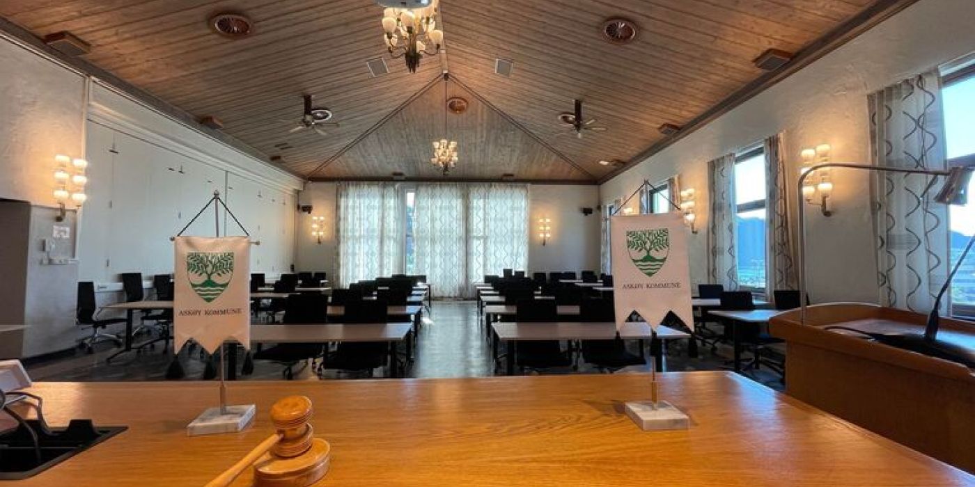 En tom sal med flere bord og stoler og ordførerklubba på bordet