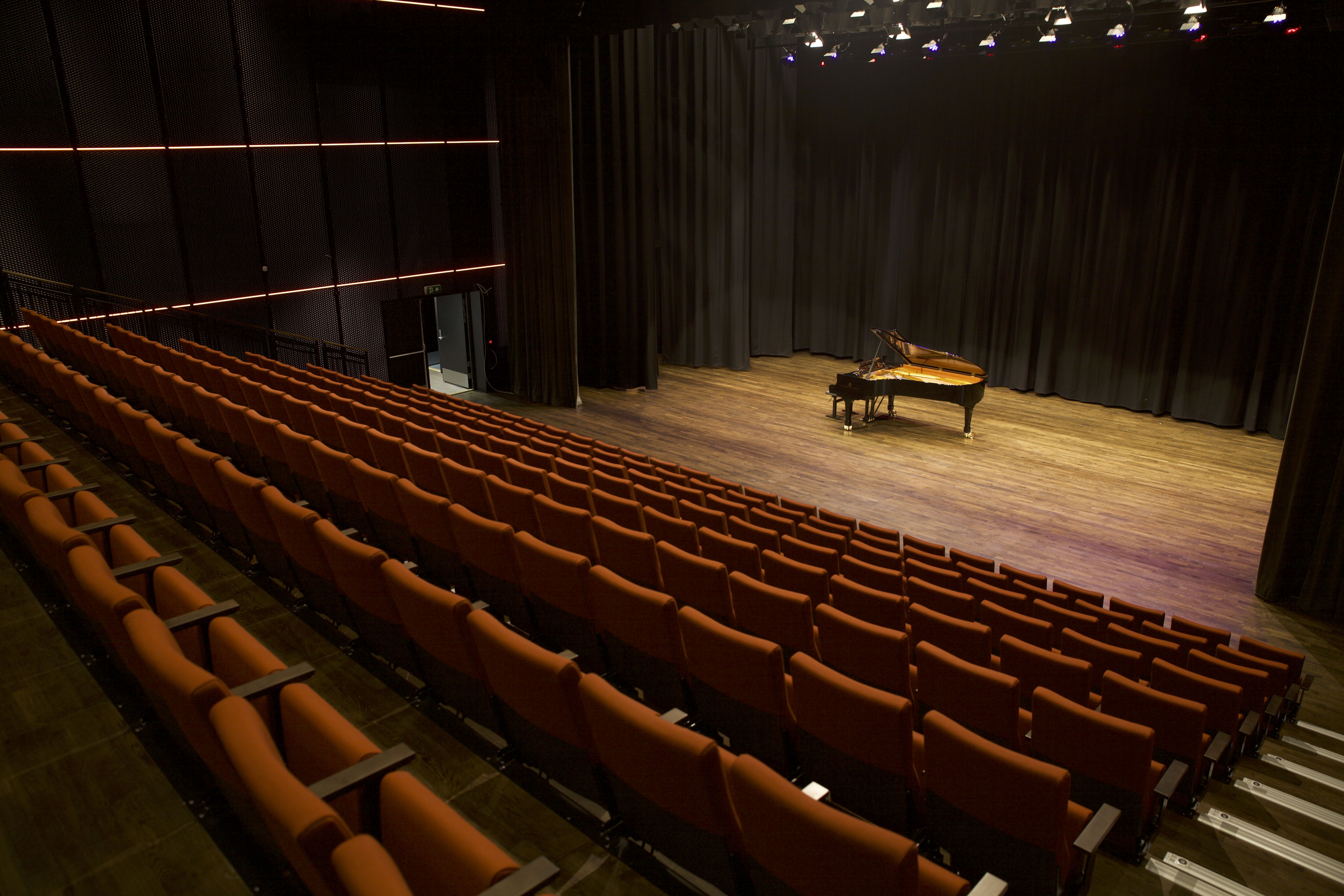 En konsert sal med et flygel på scenen og stoler i rekke i amfi