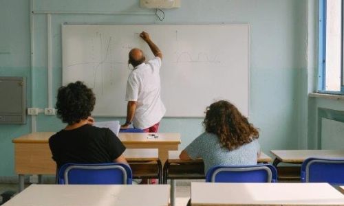 Lærer som skriver på tavle mens to voksne elever følger. Er
